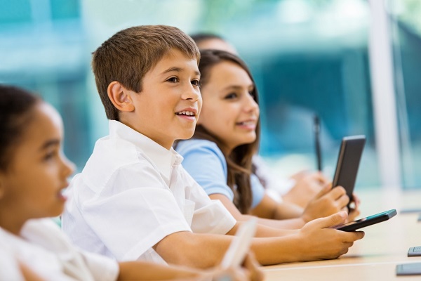 Four children sitting in the class room, having smart phone in their hands and learning something curiously.