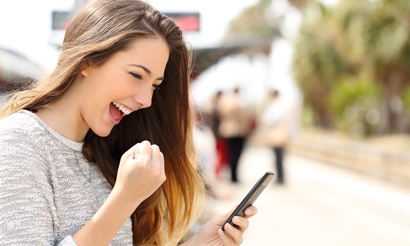 The image shows a teen girl holding her smart phone in a happy manner.