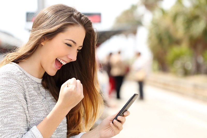 The image shows a teen girl holding her smart phone in a happy manner.